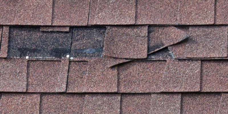 Close-up of brown roof shingles with a missing one, showing the underlying material.