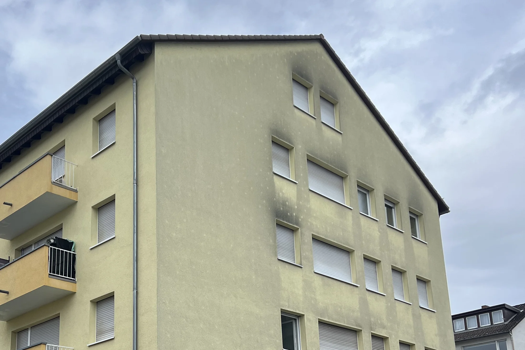 Giebelwand eines Mehrfamilienhauses mit Grünbelag und dunklen Ablaufspuren vor der Reinigung