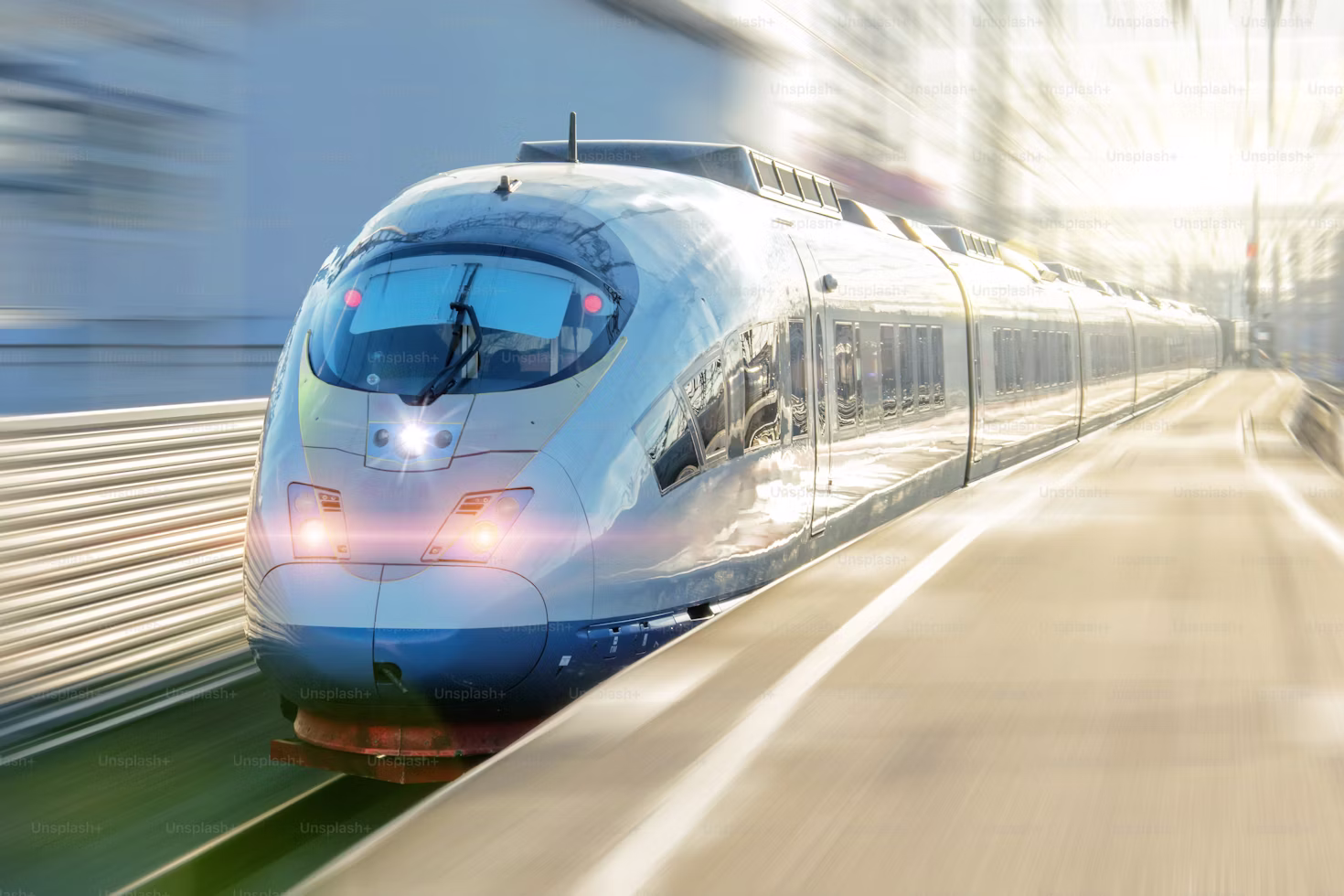 Modern high-speed train with headlights on moving rapidly on railway tracks beside a platform.