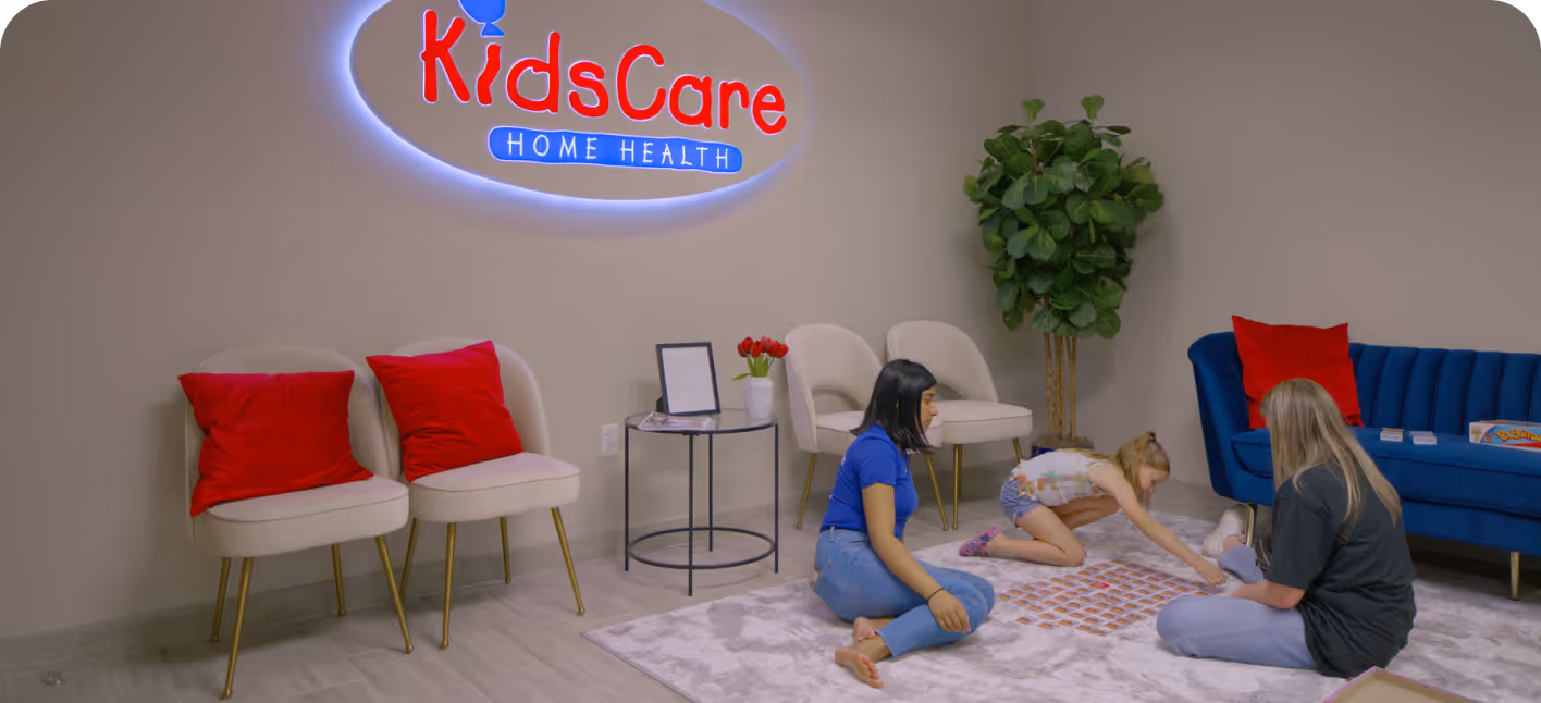Three people sitting on a carpet playing a game under an illuminated KidsCare Home Health sign.