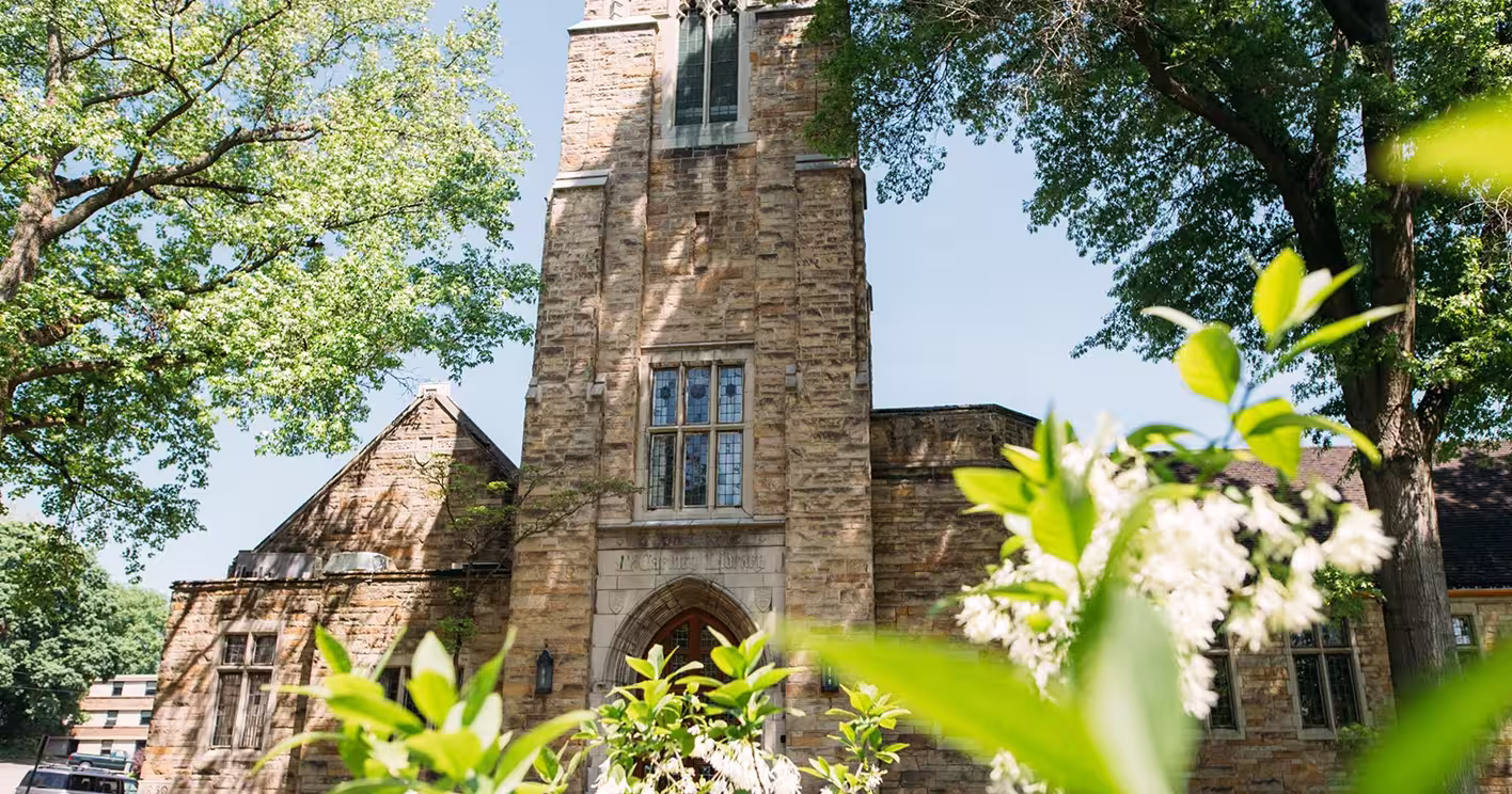 Stone building with arched doorway surrounded by trees and white flowering shrubs.