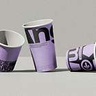 Three purple paper cups with black text arranged on a gray surface, two upright and one tipped over.