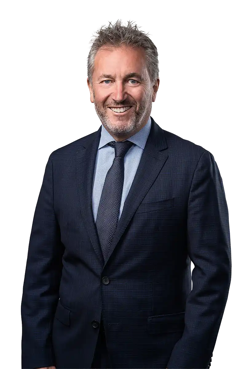Smiling man with grey hair and beard wearing a navy suit, light blue shirt, and dark tie.