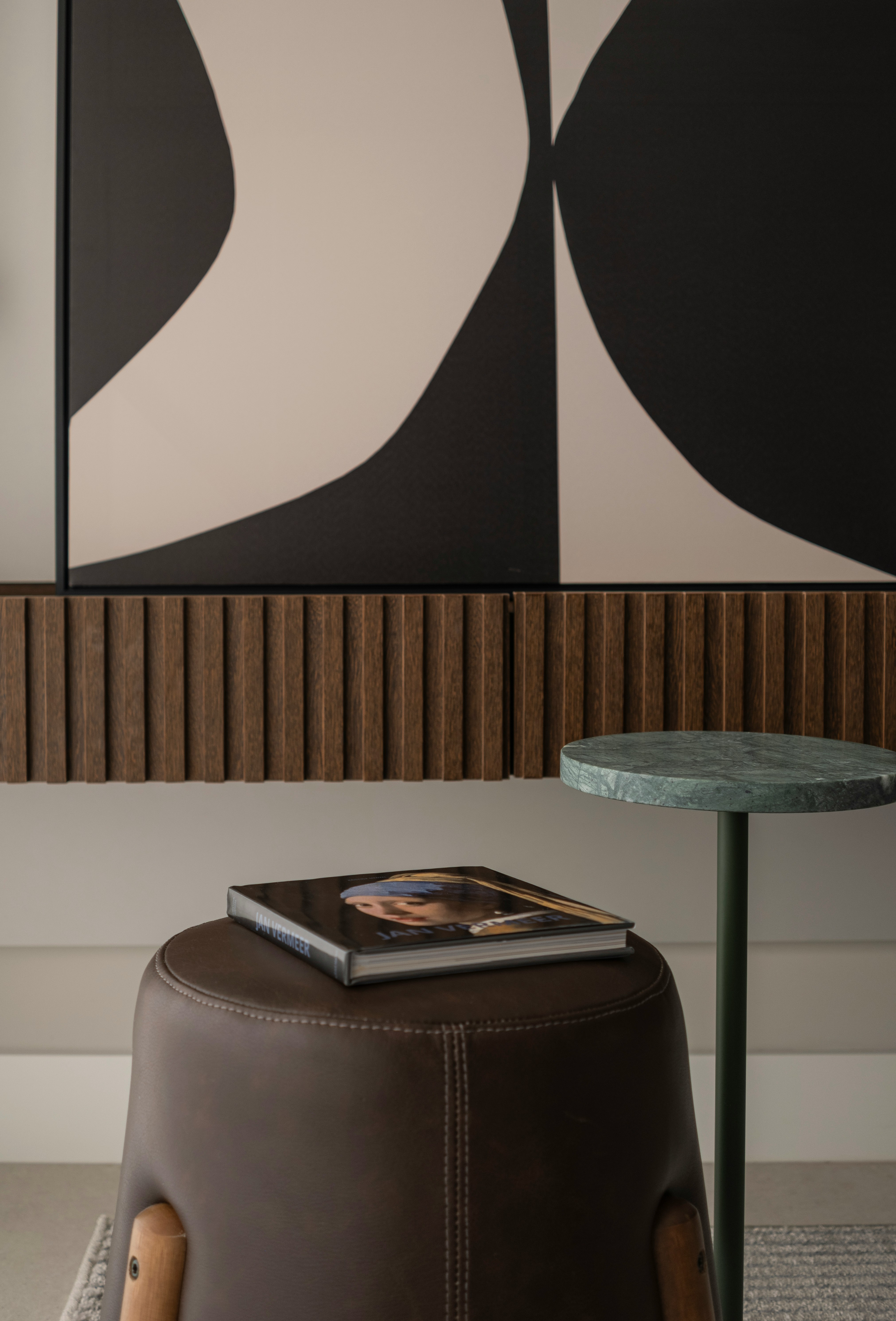 Book on Jan Vermeer on a brown leather stool beside a small green marble top table under abstract wall art.