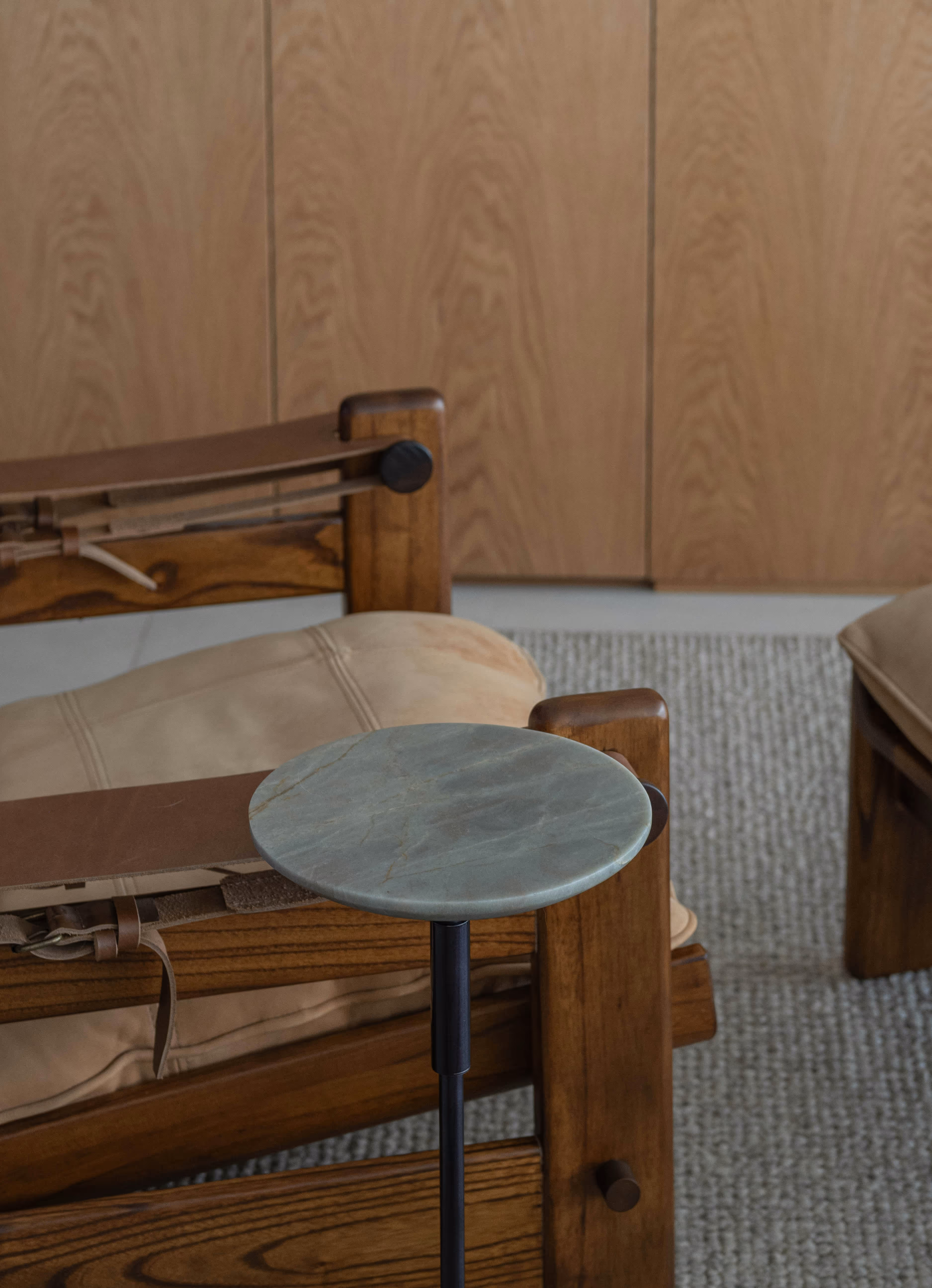 Round marble side table with black metal stand beside a wooden chair with beige cushions.