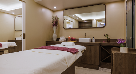 Calm spa room with massage table, candles, towels, flowers, and large wall mirror.