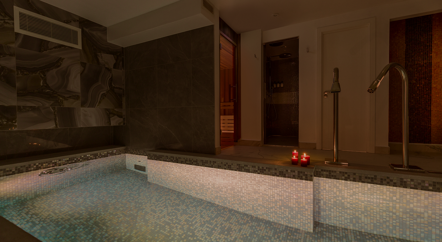 Indoor spa with mosaic tiled pool, ambient lighting, candles, and modern water fixtures.