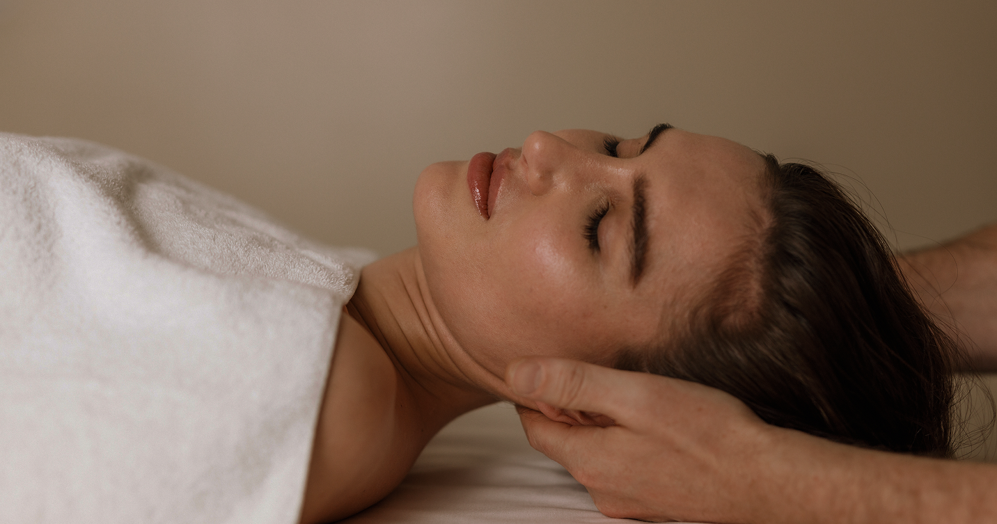 Woman receiving gentle neck massage with white towel covering her shoulder.