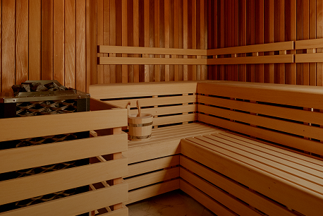 Interior of a wooden sauna room with benches, a bucket, and a heater with stones.