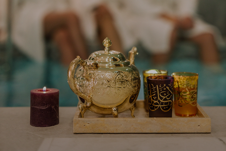 Ornate golden teapot and two decorated glasses on a tray next to a lit dark purple candle.