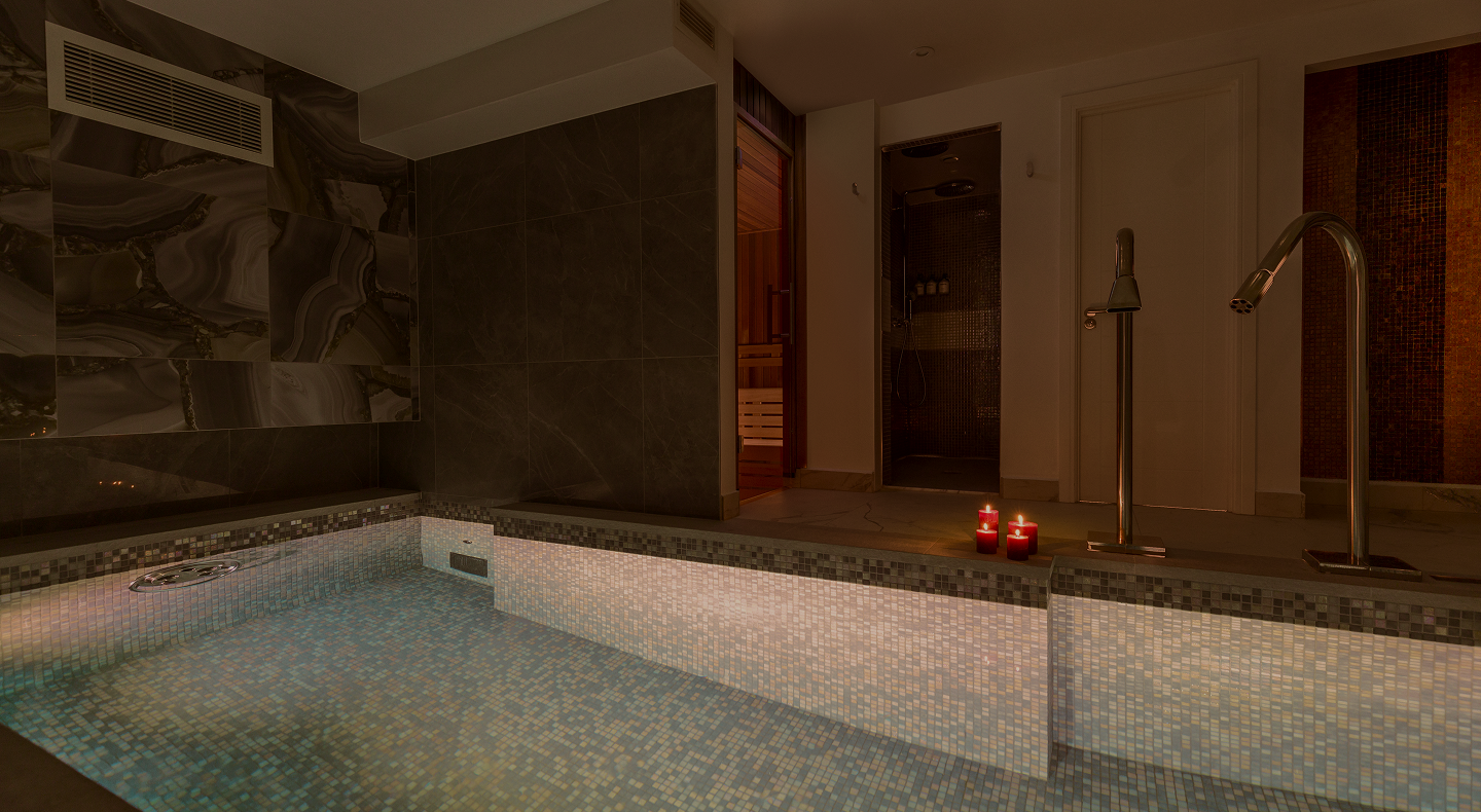 Indoor spa pool with mosaic tiles beside sauna and shower rooms, lit by three red candles.