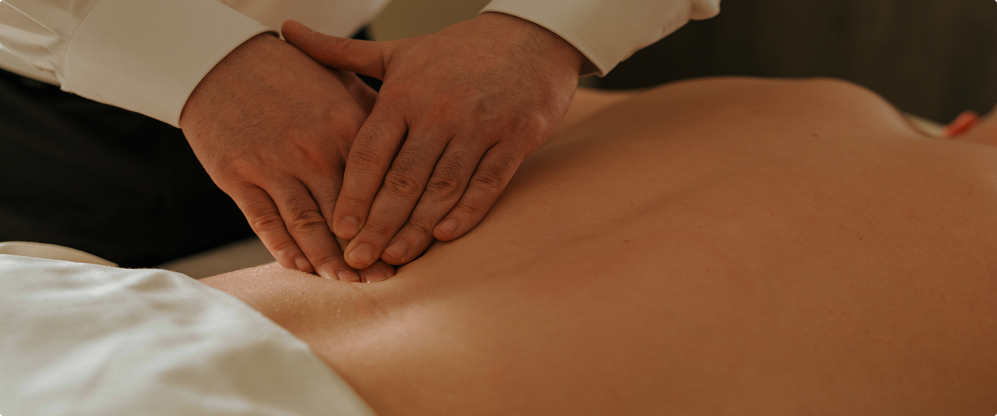 Hands giving a massage on a bare back covered partly by a white sheet.