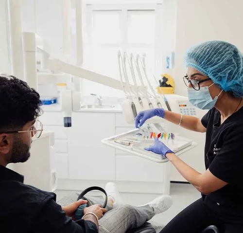Dentist wearing protective gloves, mask, and hair cover, preparing dental tools for a patient in a clinic.