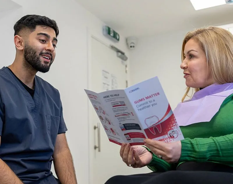 Dentist explaining dental care brochure about gums to a seated female patient wearing a purple dental bib.