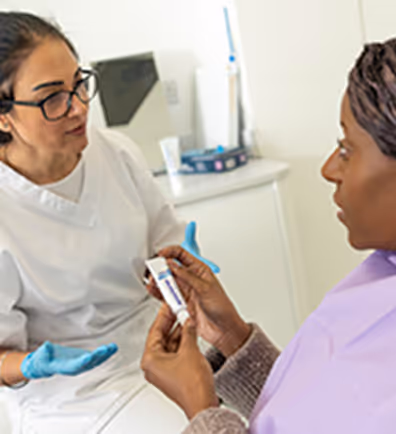 Healthcare professional in gloves explaining medication to a patient holding a pill bottle.
