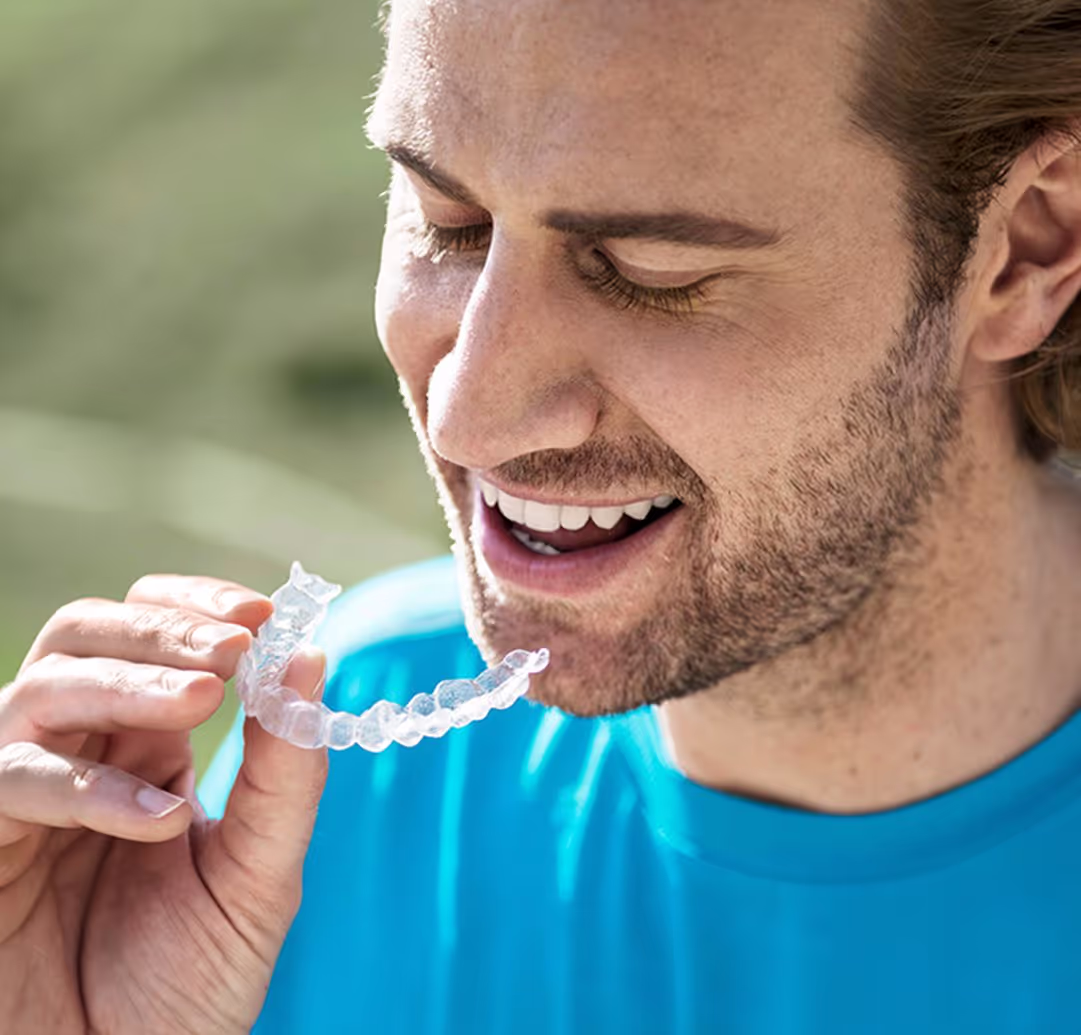 Smiling man holding a clear dental aligner near his mouth.