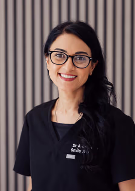 Smiling woman with long dark hair and glasses wearing a black medical scrub top.