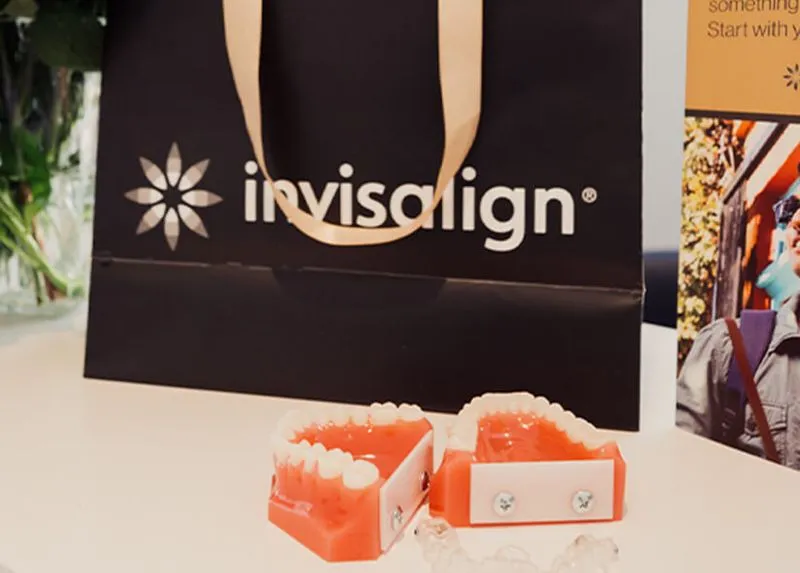 Dental models of teeth placed on a table with an Invisalign branded paper bag in the background.
