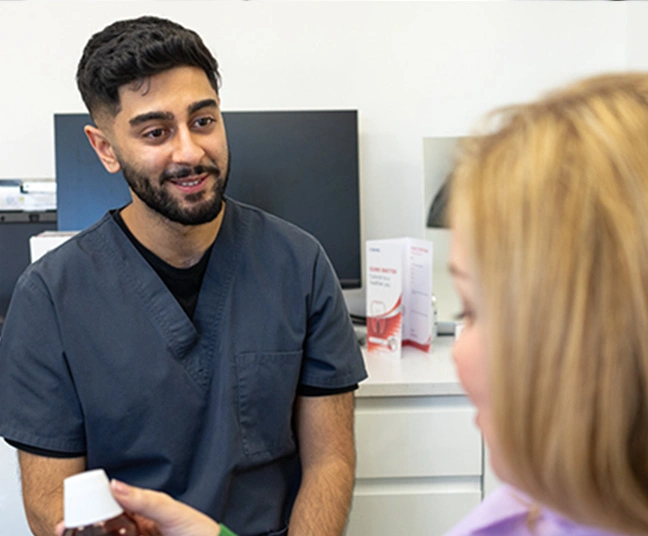 Male healthcare professional in scrubs talking to a seated woman who is holding a medicine bottle.