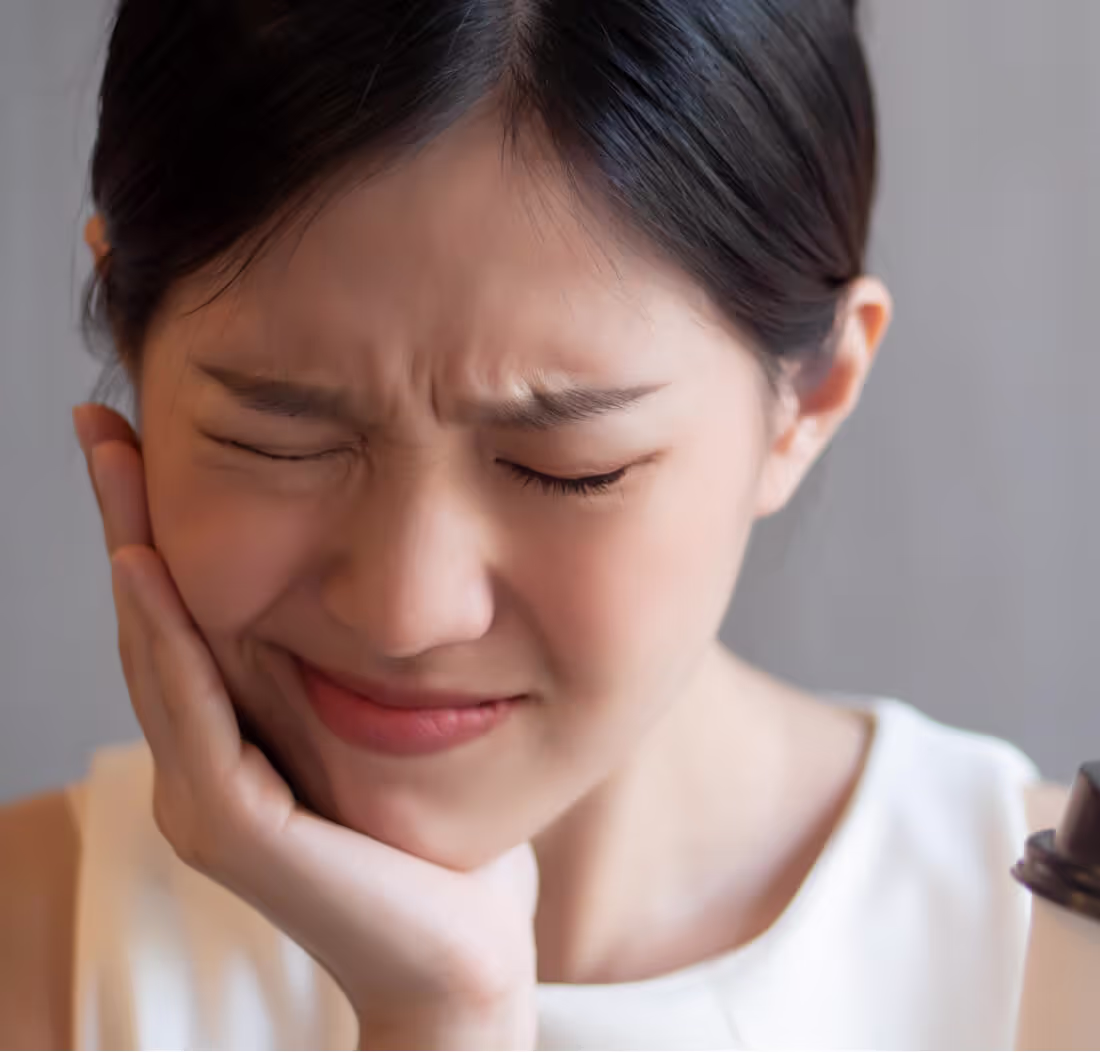 Woman with eyes closed, grimacing in pain while holding her cheek.