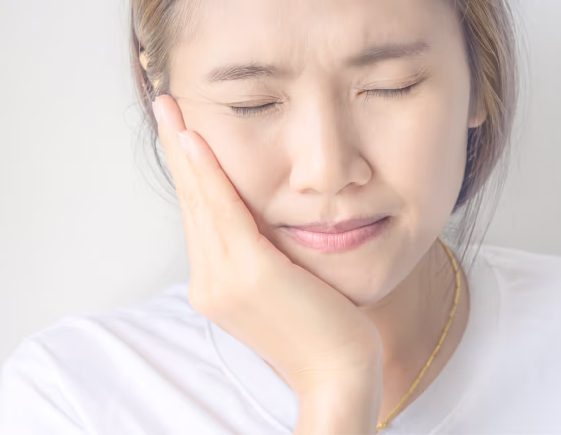 Woman with eyes closed holding her cheek in pain, indicating a toothache or dental discomfort.