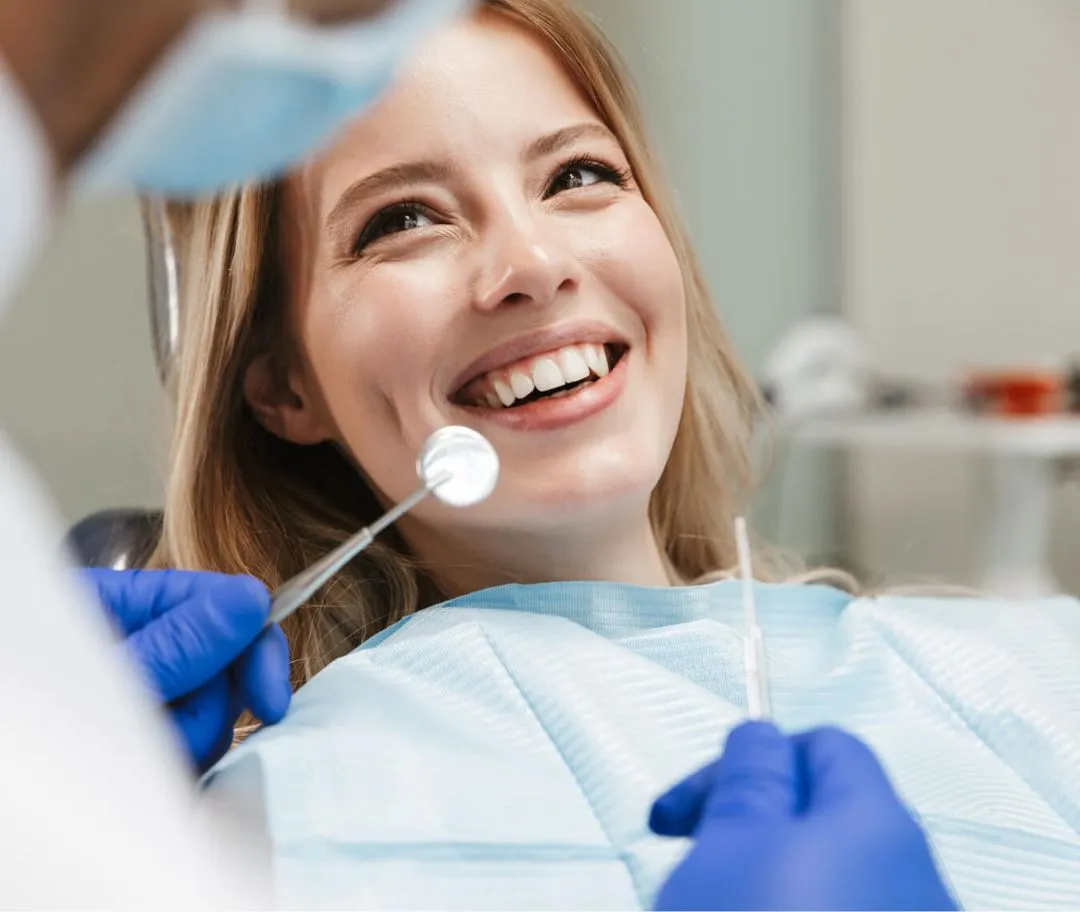 Smiling woman in dental chair during a dental checkup with a dentist holding dental tools.