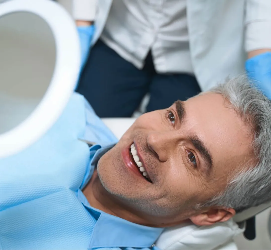 Smiling middle-aged man with gray hair lying in a dental chair wearing a blue dental bib.