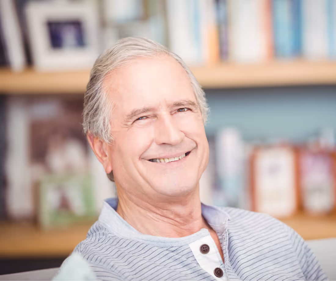 Smiling elderly man with gray hair wearing a striped henley shirt in a cozy room.