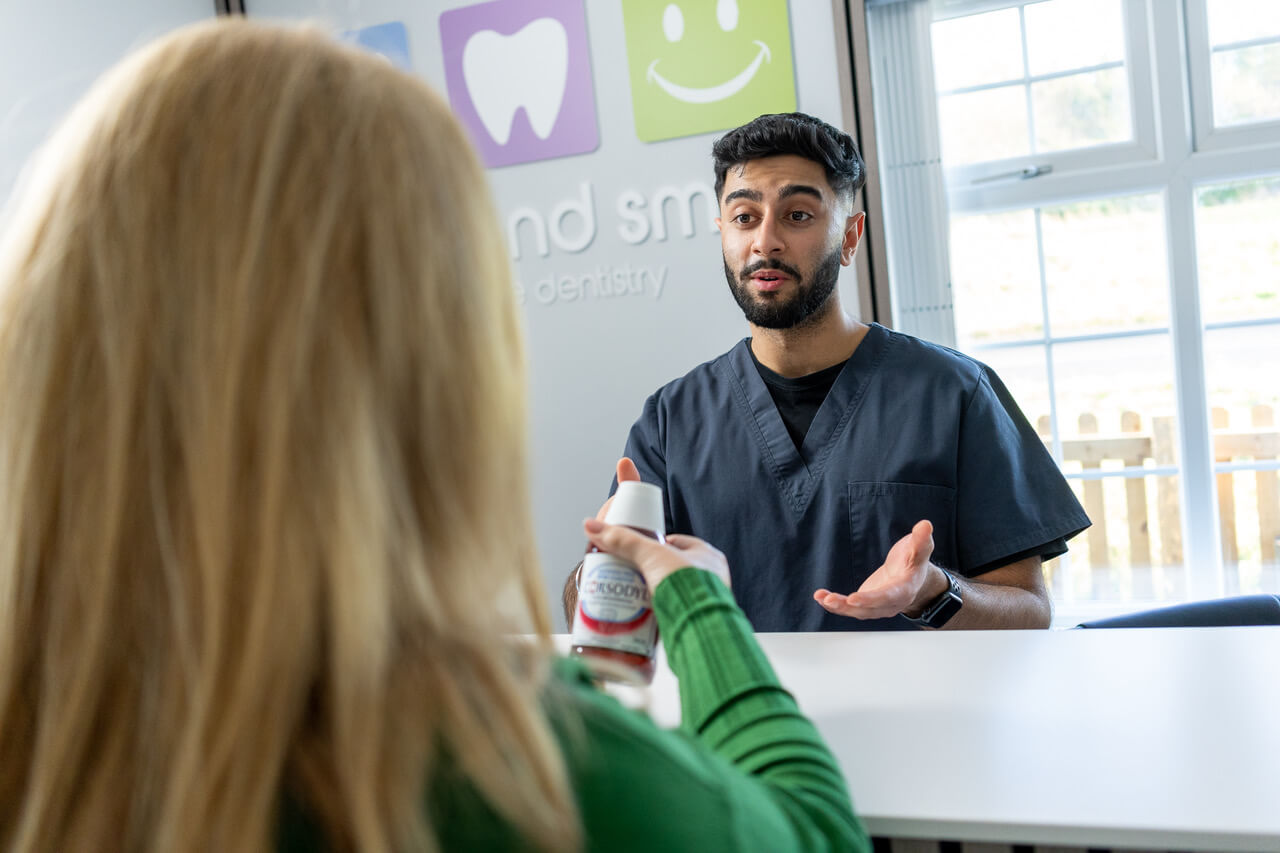 Dentist explaining mouthwash to a patient sitting across the table at a dental clinic.