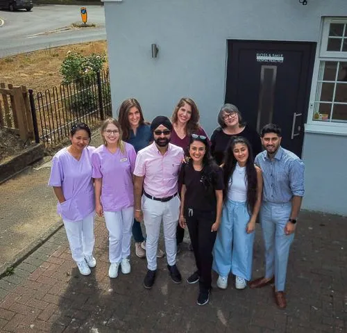 Group of nine diverse smiling adults standing outside a building with a door labeled Floss & Smile Dental Practice.