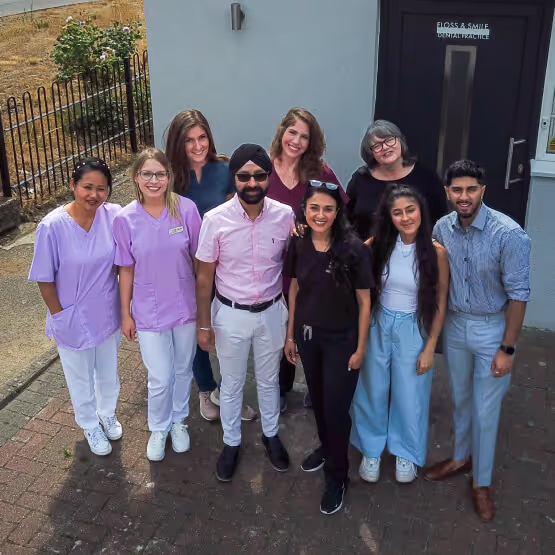 Group of nine smiling dental professionals standing outside a dental practice entrance.