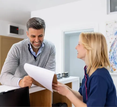 Smiling receptionist handing documents to a male visitor at an office reception desk.