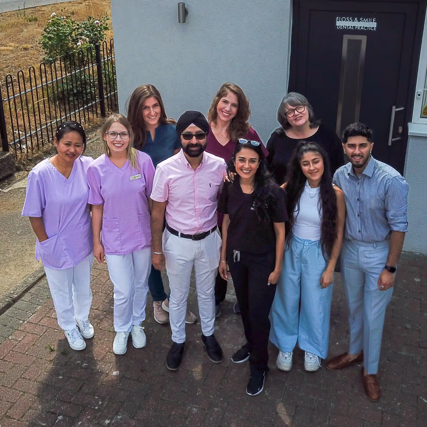 Group of nine diverse dental professionals smiling outside the entrance of Floss & Smile dental practice.