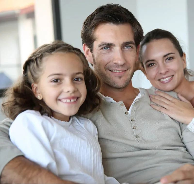 Smiling family of three with a man, woman, and young girl sitting closely together indoors.