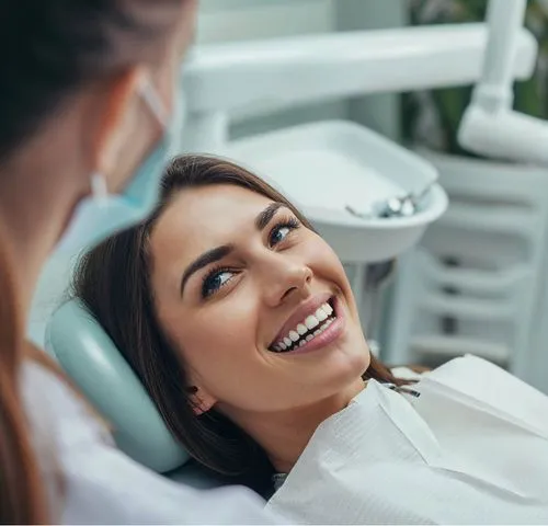 Smiling woman reclining in a dental chair looking up at a masked dentist.