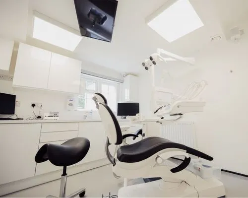 Modern dental clinic room with black and white dental chair, stool, computers, and bright overhead lights.