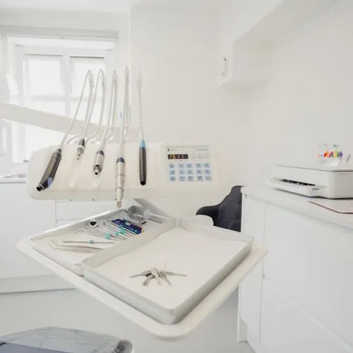 Dental workstation with handpieces, dental tools, and sterilization equipment in a bright clinic room.