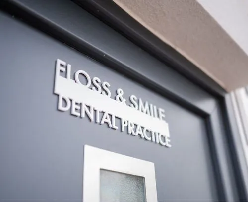 Blue door with raised white letters reading 'FLOSS & SMILE DENTAL PRACTICE'.