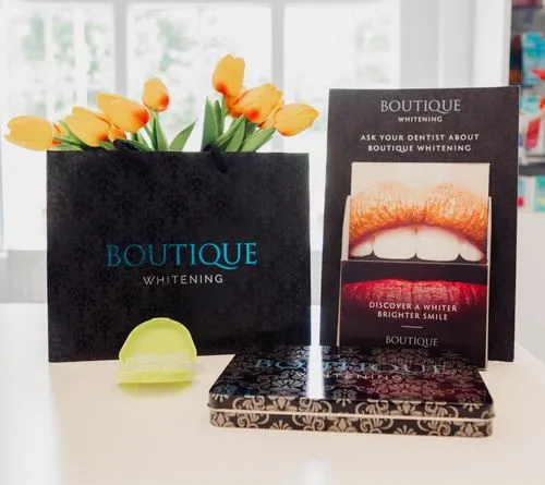 Boutique Whitening branded black bag with yellow tulips, a teeth whitening tray, and promotional display with bright smile image.