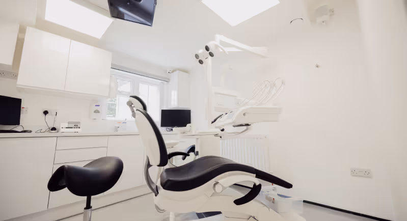 Modern dental clinic room with a black and white dental chair, dentist stool, and computer monitors.