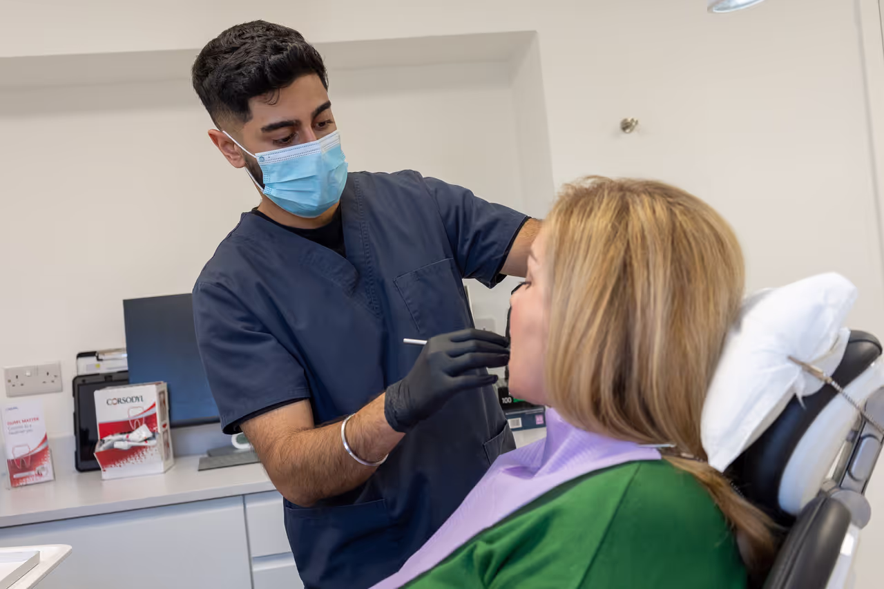 Dentist wearing a blue uniform and face mask examining a female patient seated in a dental chair.