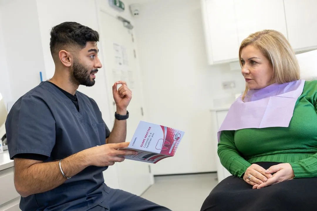Dentist in scrubs explaining gum health using a pamphlet to a woman wearing a dental bib in a clinic.
