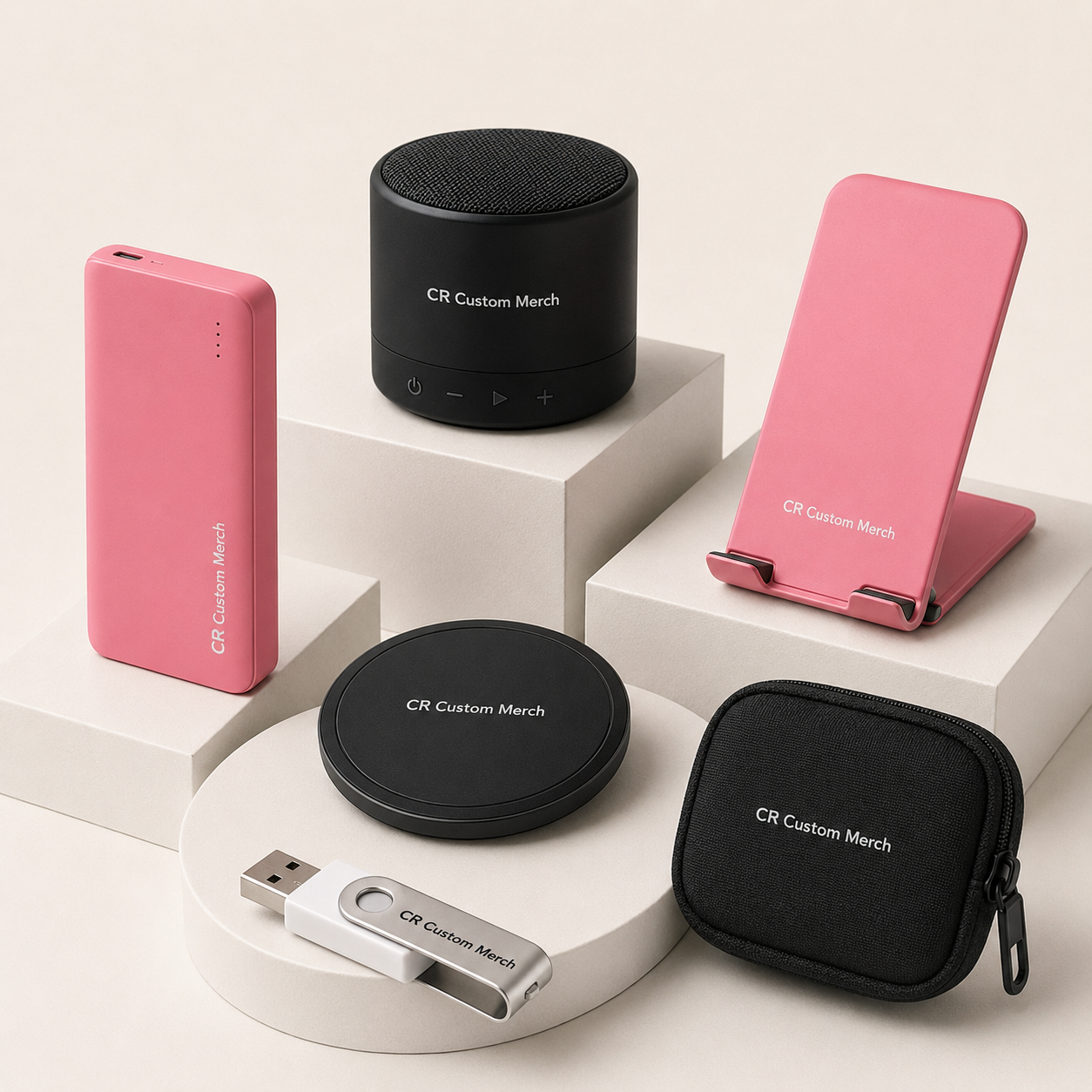 CR Custom Merch branded speaker, power bank, USB drive, charging pad, phone stand and cable pouch in a studio display