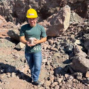 Image of Geologist, Jeandro Vitorio, holding a rock at a quarry. Background shows boulders and rocks broken down.