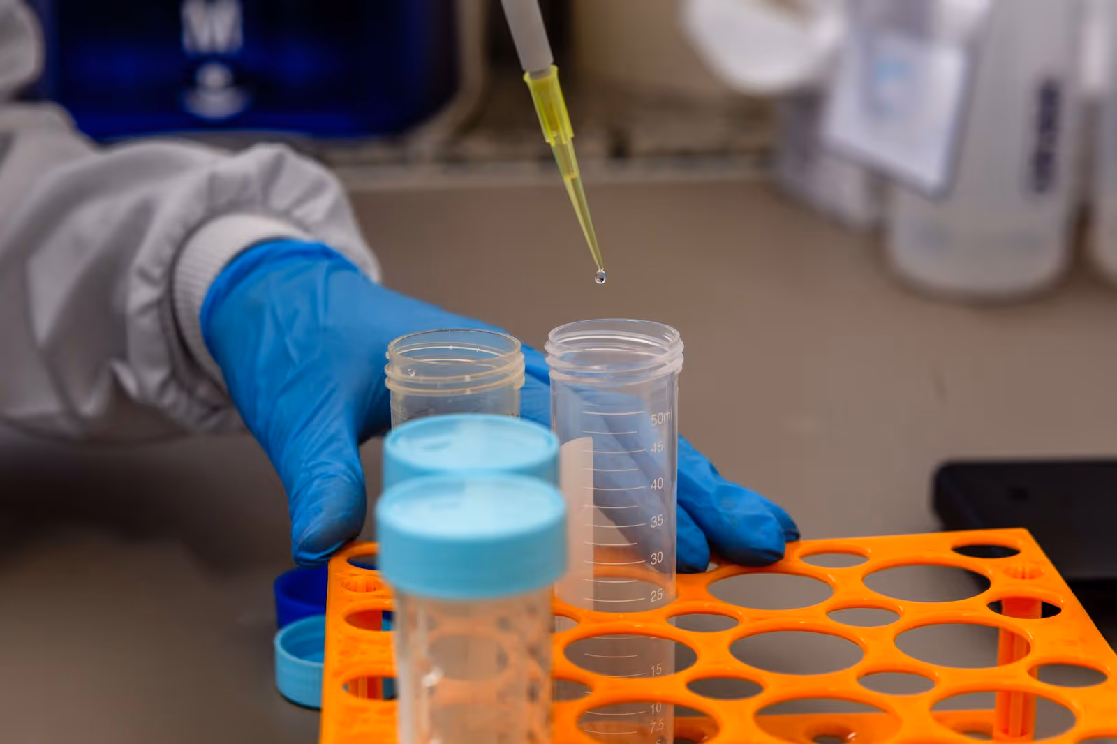 Gloved hand pipetting a droplet into measuring vials in a lab
