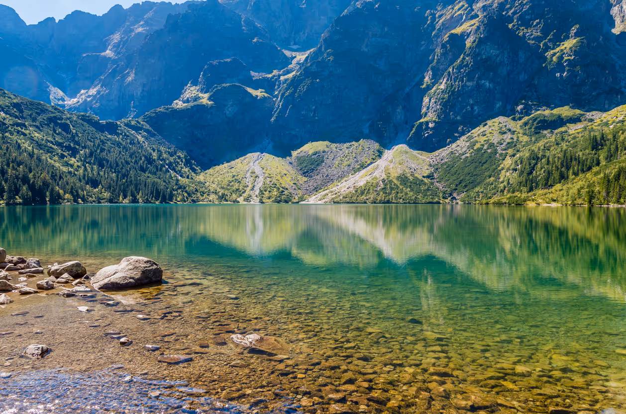 Clear mountain lake reflecting forested slopes and rocky peaks, illustrating natural systems that support Earth's carbon cycle.