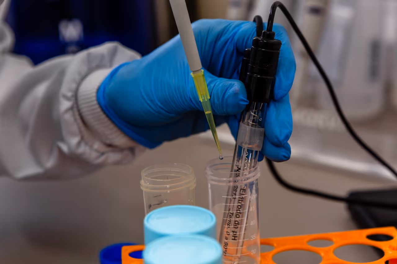 Hand weating blue glove holding a pH-meter and pipetting water with the other hand
