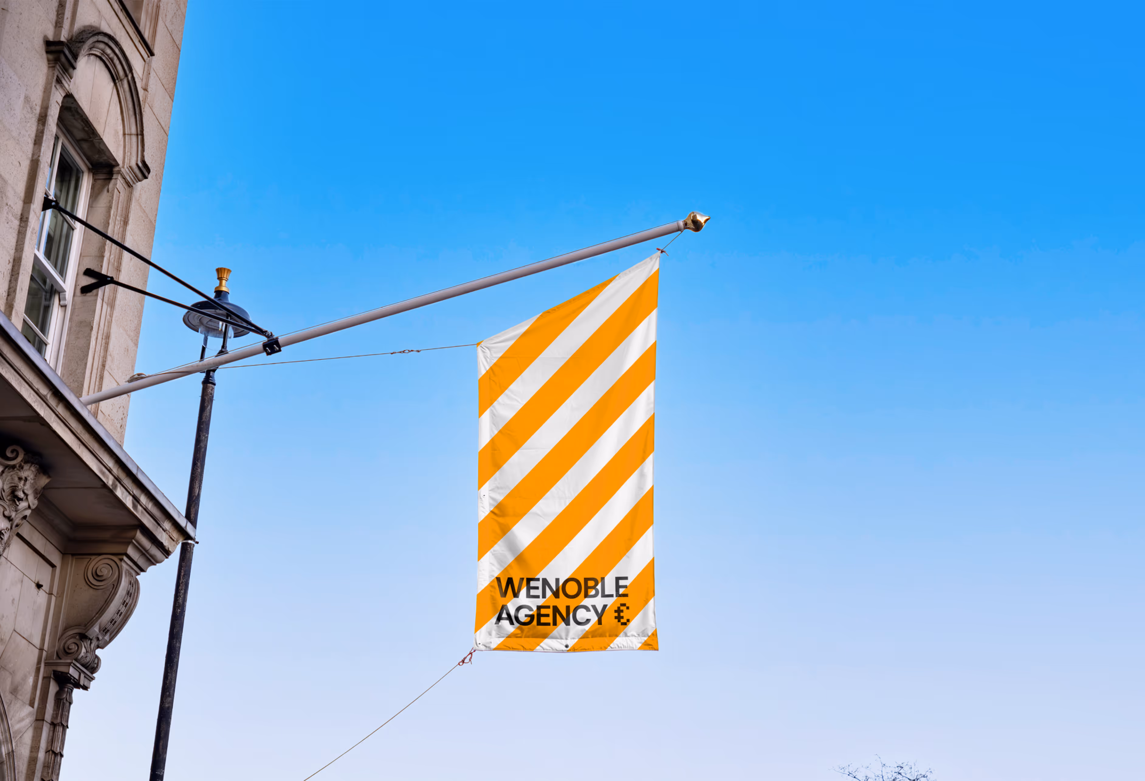 Flag with diagonal orange and white stripes and text ‘Wenoble Agency’ hanging from building.
