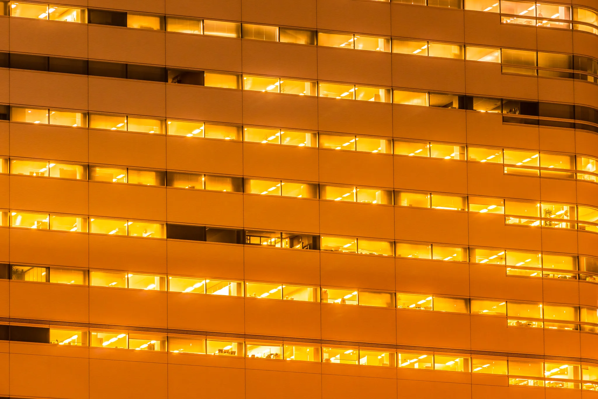 Close-up of a modern office building exterior at night with warm lights glowing through windows.