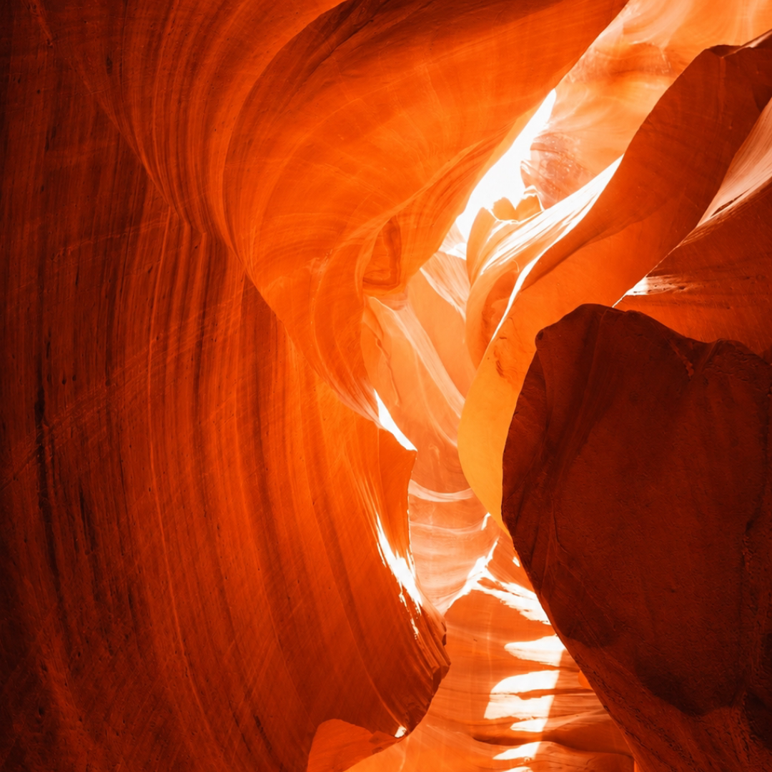Sunlight shining through smooth, curved orange sandstone walls of a slot canyon.